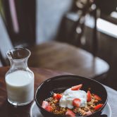 bowl of cereal with strawberries beside glass of milk on table