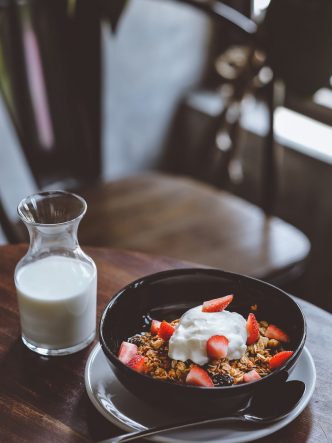 bowl of cereal with strawberries beside glass of milk on table