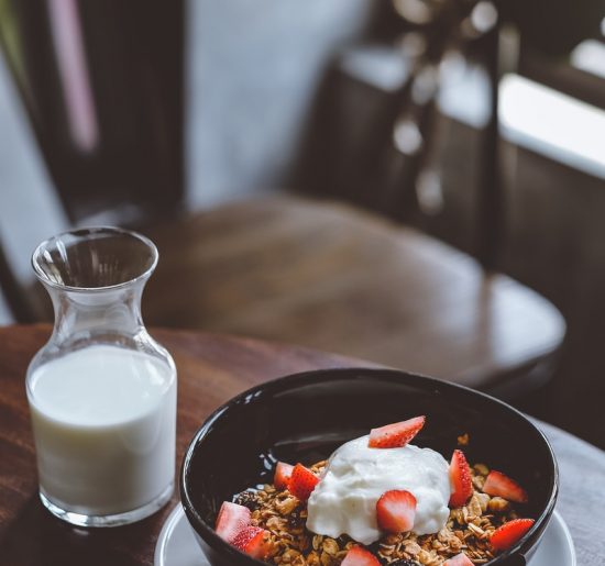 bowl of cereal with strawberries beside glass of milk on table