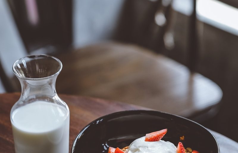 bowl of cereal with strawberries beside glass of milk on table