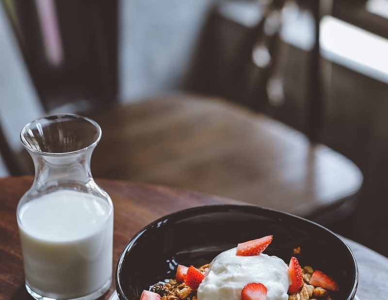 bowl of cereal with strawberries beside glass of milk on table