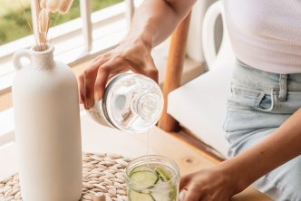 woman in white tank top pouring water on clear drinking glass