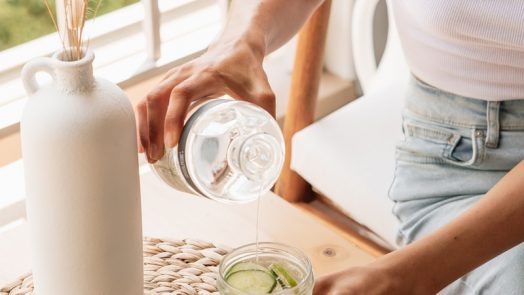 woman in white tank top pouring water on clear drinking glass