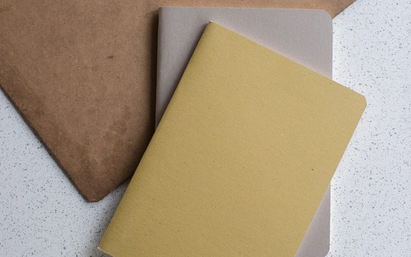 yellow and gray softbound book near brown clip board